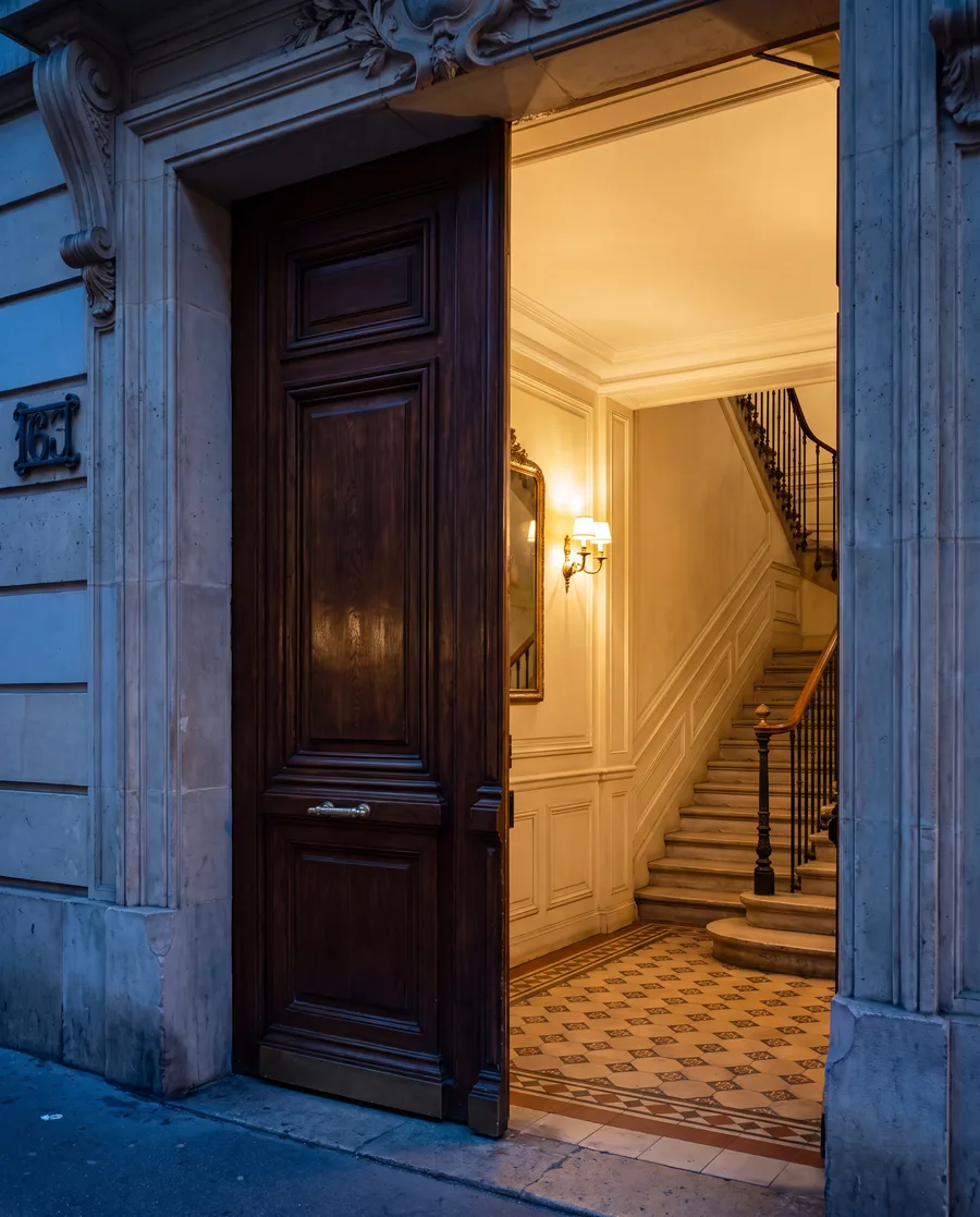 Porte cochère haussmannienne entrouverte sur un hall d'entrée parisien éclairé